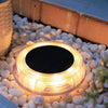 Round solar deck light glowing warm white on timber decking