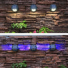 Butterfly-shaped solar wall light glowing in colour on a garden fence